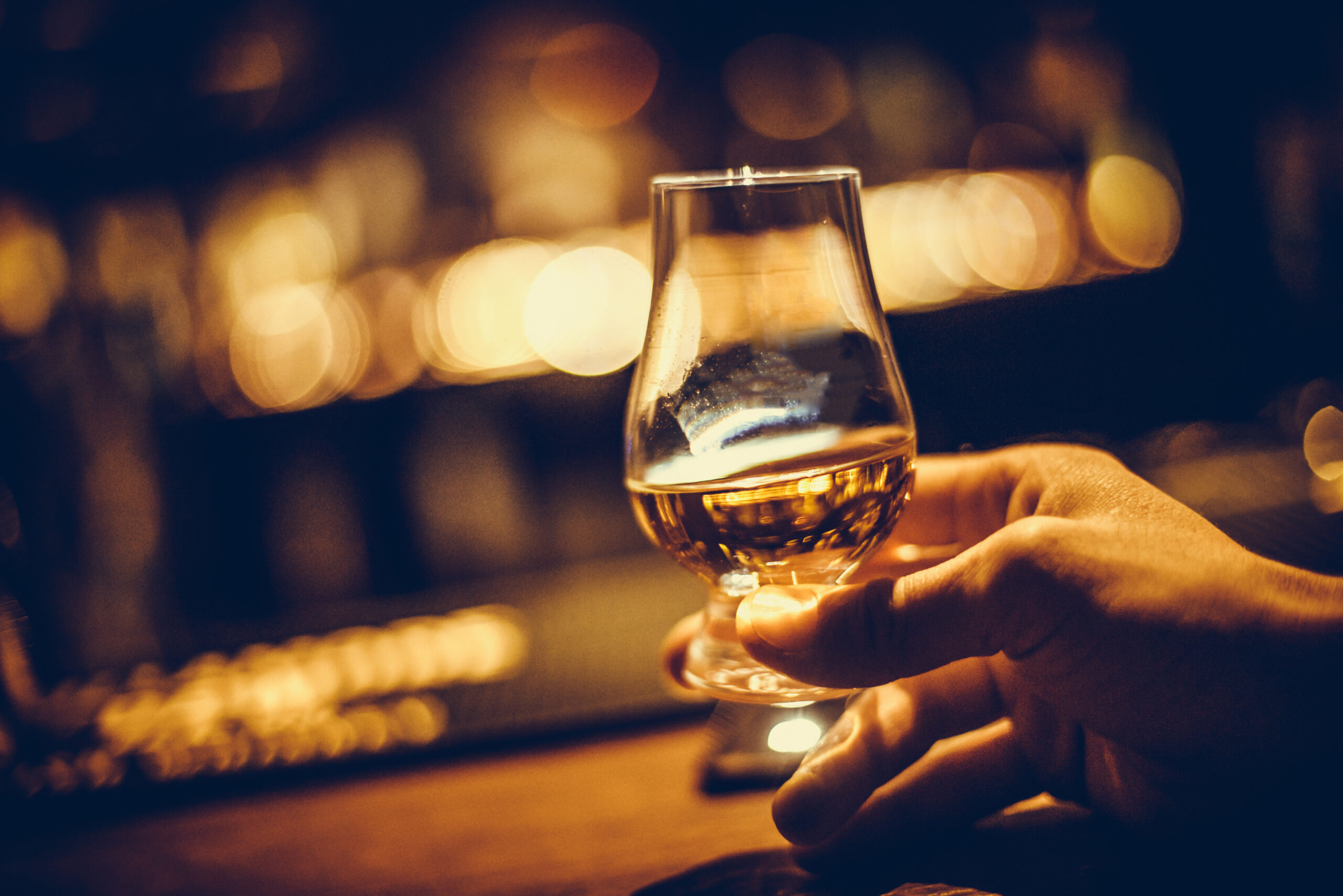 Close up shot of a hand holding a Glencairn single malt whisky glass.